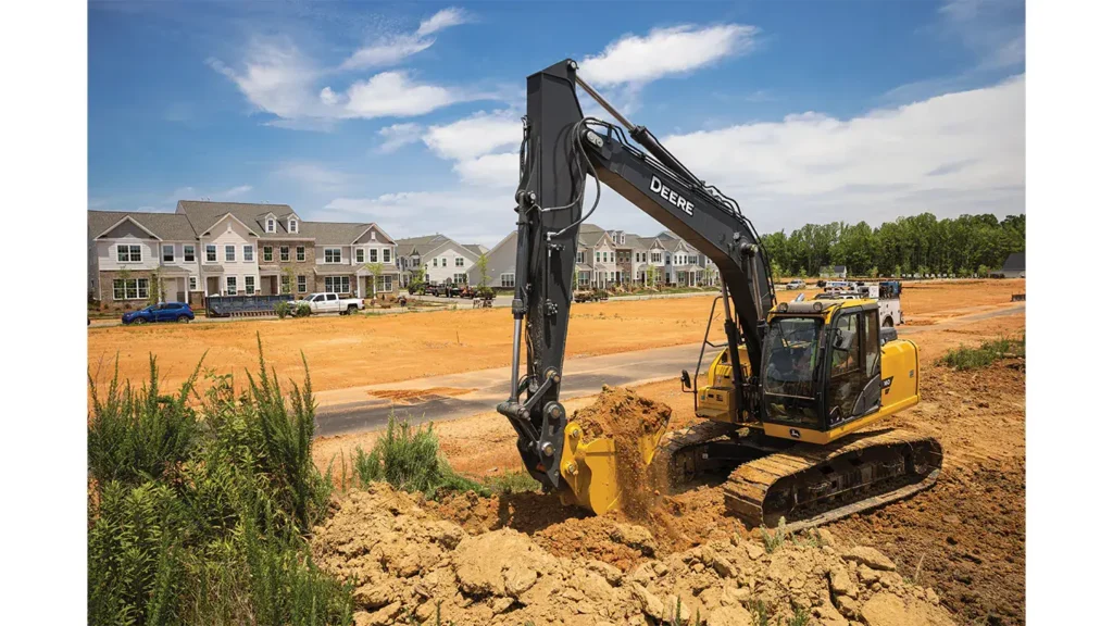 A John Deere excavator digging into a dirt pile at a construction site.