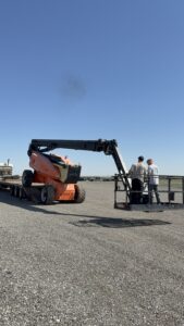 125ft Articulating Boom Lift with workers operating elevated platform equipment at an outdoor job site under clear blue skies.