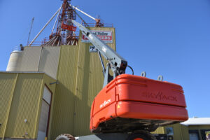 85ft Telescopic/Straight Boom Lift providing elevated access for industrial maintenance work on a grain facility under clear blue skies.